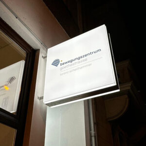 Bild des beleuchteten Leuchtkasten mit Logo am Eingangsaufgang zum Bewegungszentrum Goethestrasse.